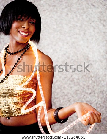 Portrait of a beautiful black woman holding Christmas fairy lights around her neck and smiling against a silver glitter background.