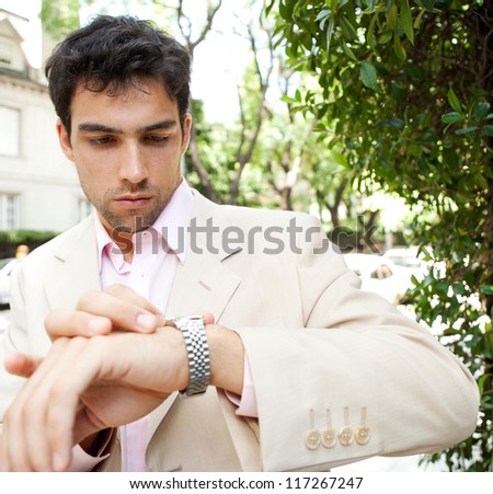 Close up of a young attractive businessman looking at the time in his watch while standing in a classic city street, outdoors.