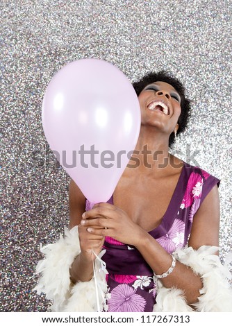 Attractive young black woman holding pink balloons against a silver glitter background, laughing.