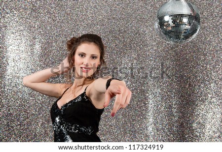 Attractive young woman dancing in a night club with a mirror ball and a silver background.