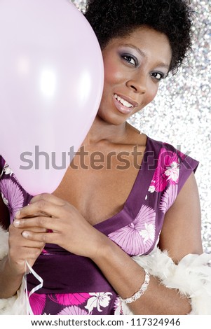 Close up portrait of an attractive young black woman holding pink balloons against a silver glitter background, smiling.