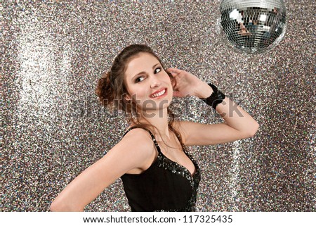 Attractive young woman dancing in a night club with a mirror ball and a silver background.