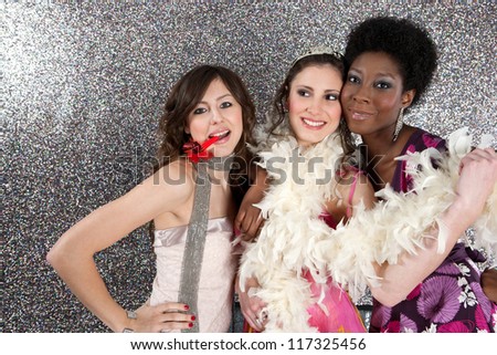 Portrait of three young women having a party and blowing whistles against a silver background.