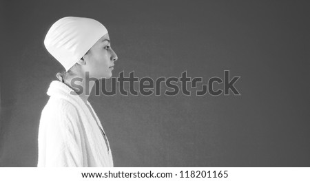 Panoramic format portrait of a young woman swimmer wearing a white robe and rubber hat, standing against a dark background.