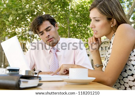 Two business people having a meeting and using technology outdoors, while having a coffee in a coffee shop terrace.