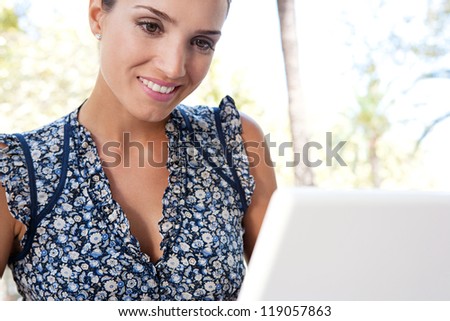 Close up view of a young attractive businesswoman using a laptop computer while outdoors in a city with palm trees, smiling.