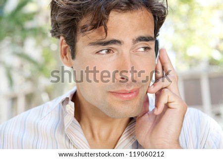 Portrait of a young attractive businessman using a hands free device to have a conversation on his cell phone while standing in front of classic office buildings in the city.