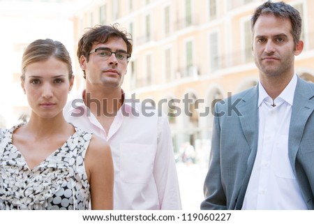Three strong business people standing together next to a classic office building in the city on a sunny day.