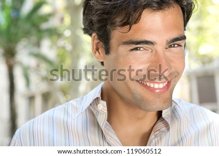 Young attractive businessman using a hands free device to have a conversation on his cell phone while standing in front of classic office buildings in the city, smiling.