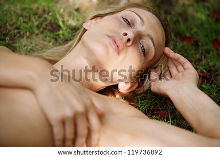Over head view of a beautiful naked woman laying down on green grass, covering herself with her hand and relaxing in nature.