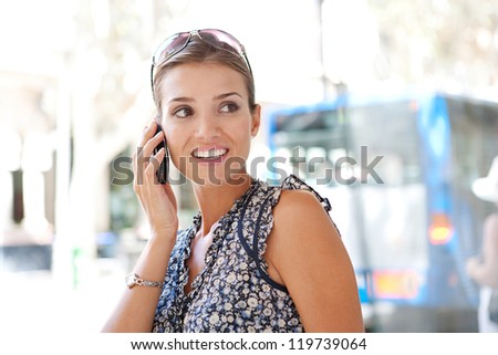 Portrait of an attractive commuting businesswoman using her smart phone in the city near a bus stop.