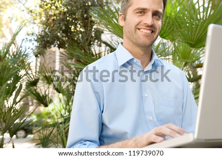 Senior businessman using a laptop computer while sitting on a bench in a city park, outdoors.