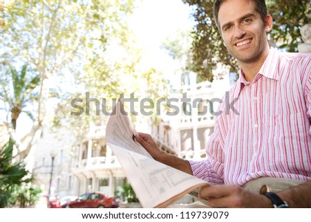 Senior businessman reading a newspaper while sitting down in a classic city square, outdoors.