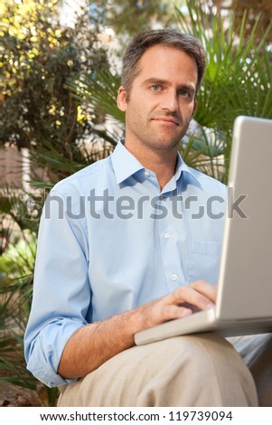 Senior businessman using a laptop computer while sitting on a bench in a city park, outdoors.