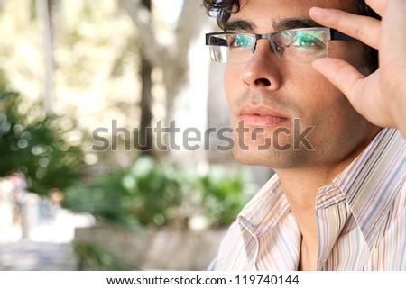 Close up portrait of a young and attractive businessman looking up while holding his reading glasses with his hand.