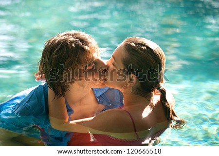Close up of a sexy young couple submerged in a swimming pool while dressed, hugging and kissing while on a tropical destination vacation.