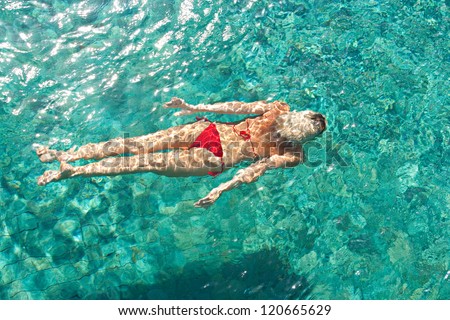 Over head rear view of an attractive young woman swimming under water and wearing a red bikini while on vacation.