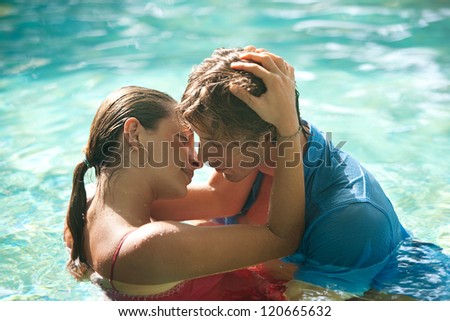 Close up of a sexy young couple submerged in a swimming pool while dressed, hugging and kissing while on a tropical destination vacation.