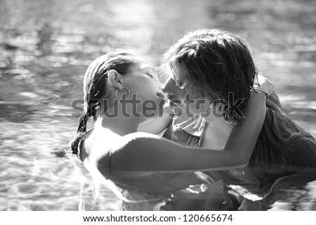 Black and white close up view of a sexy young couple submerged in a swimming pool while dressed, hugging and kissing while on a tropical destination vacation.