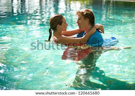 Sexy young couple submerged in a swimming pool while dressed, hugging and kissing while on a tropical destination vacation.