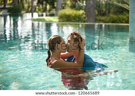 Sexy young couple submerged in a swimming pool while dressed, hugging and kissing while on a tropical destination vacation.