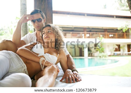 Young and attractive sexy couple lounging on a tropical garden bed in an exotic hotel spa garden, relaxing next to a swimming pool.