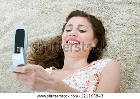 Over head view of a young and beautiful hispanic woman laying down on a furry carpet at home, using a cell phone in the living room,