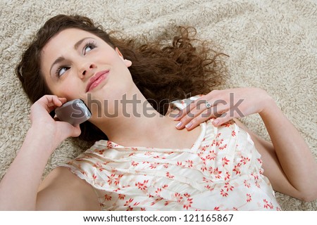 Over head view of a young and beautiful hispanic woman laying down on a furry carpet at home, having a cell phone conversation.