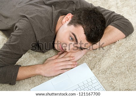 Over head view of a young hispanic man laying down on a furry carpet at home, using his laptop computer.