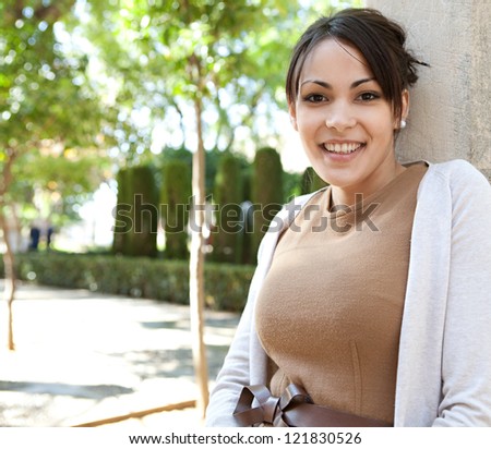 Close up portrait of an attractive young woman leaning on a column while visiting a botanic garden on a sunny day, smiling at the camera.