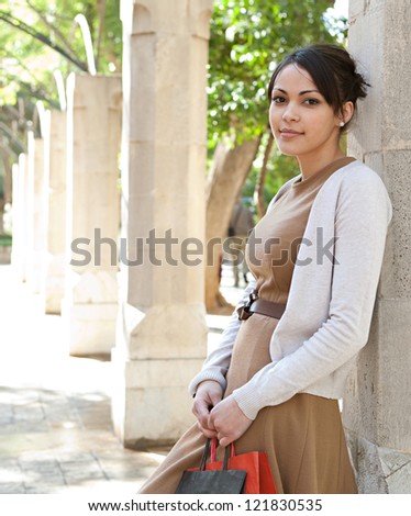 Portrait of an attractive young woman holding her shopping bags while leaning on a stone column in a romantic garden, outdoors.
