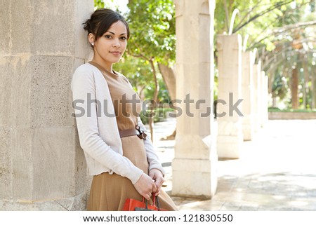 Portrait of an attractive young woman holding her shopping bags while leaning on a stone column in a romantic garden, outdoors.