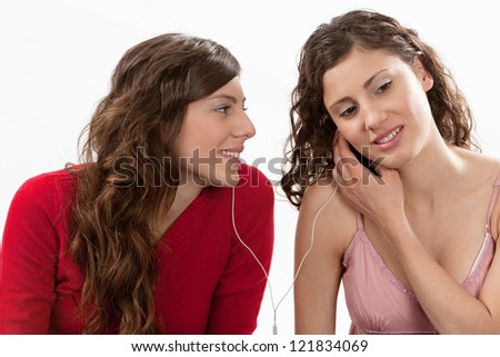 Two young women sharing their earphones and listening to music, isolated against a white background.