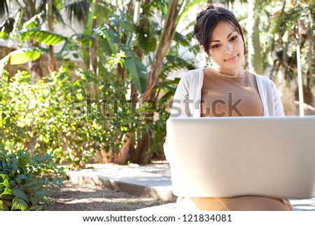 Portrait of a young professional woman using a laptop computer while sitting on a bench in a park, on a sunny day.
