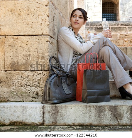 Young professional woman having a lunch break and sitting down on a park steps with her shopping bags and bottle of water.