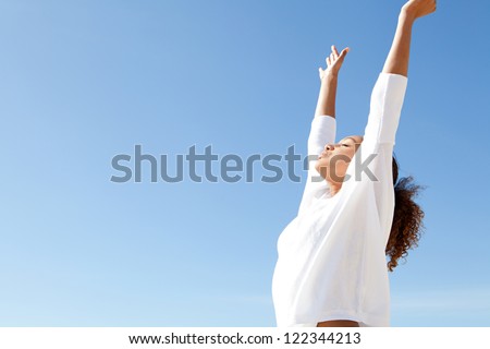 Young teenage girl breathing fresh air with her arms outstretched up and relaxing while standing against a blue sky.