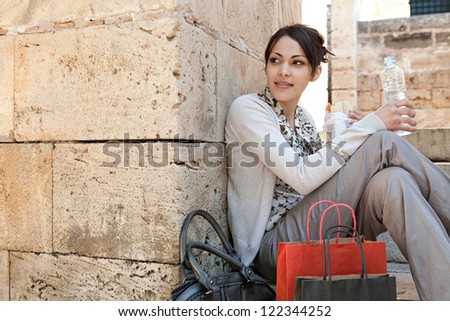Young businesswoman having a lunch break and sitting down on a park steps with her shopping bags and bottle of water.
