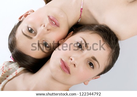 Over head beauty close up portrait of two young women with perfect skin lying next to each other, with their heads in opposite directions.