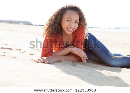 Young teenage girl relaxing on a white sand beach on a sunny day, smiling at the camera.