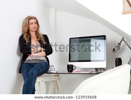Attractive professional woman sitting on her work desk being proud and successful, next to her computer screen.