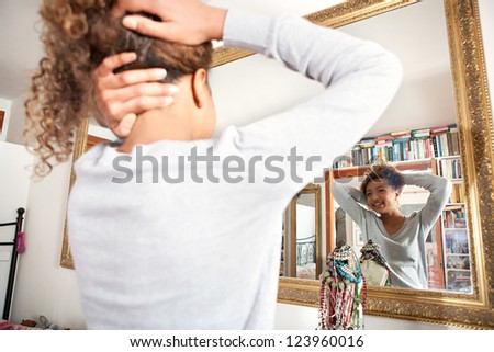Teenage girl looking at herself in the mirror, posing with a new hair style.