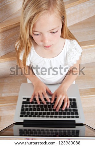 Over head close up view of a young girl child using a laptop computer while sitting on wooden steps at home.