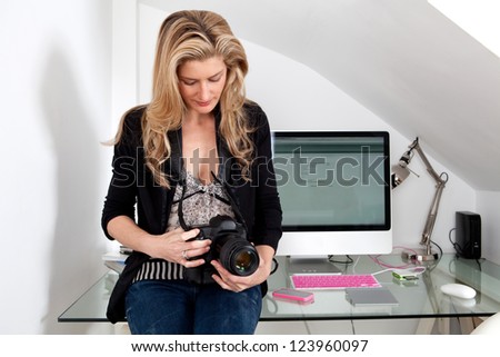 Smart businesswoman holding a professional digital photographic slr camera while sitting on her office desk.