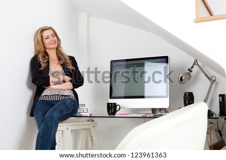 Attractive professional woman sitting on her work desk being proud and successful, next to her computer screen.