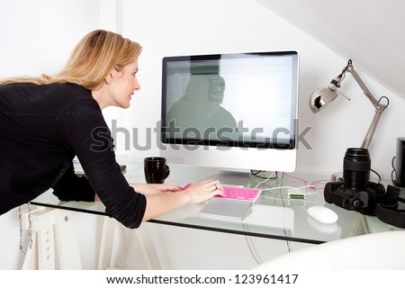 Creative photographer woman professional using a desktop computer and typing on a keyboard, busy at work with photographic equipment.