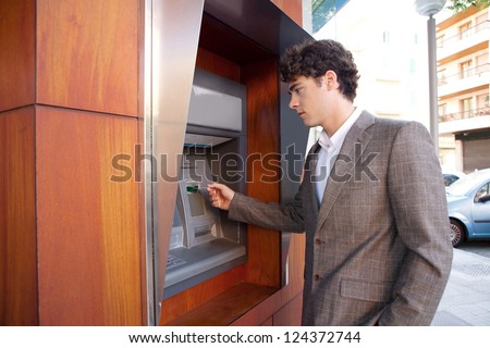Side view of an elegant businessman withdrawing money from a wood decorated bank cash point, outdoors.