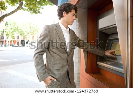 Side view of an elegant businessman withdrawing money from a wood decorated bank cash point in the city, outdoors.