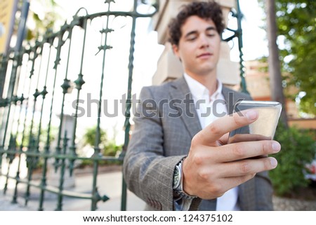 Hispanic businessman using a smart phone while standing in the corner of a classic city street with a green iron rail behind him.