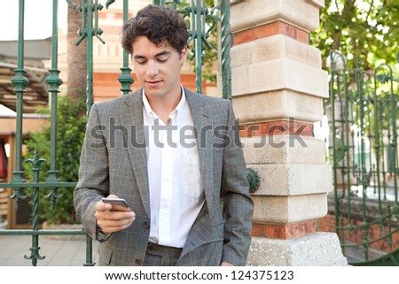Hispanic businessman using a smart phone while standing in the corner of a classic city street.