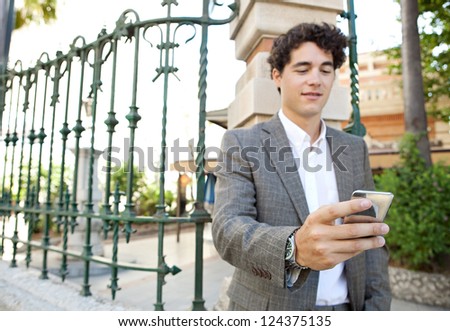 Hispanic businessman using a smart phone while standing in the corner of a classic city street.